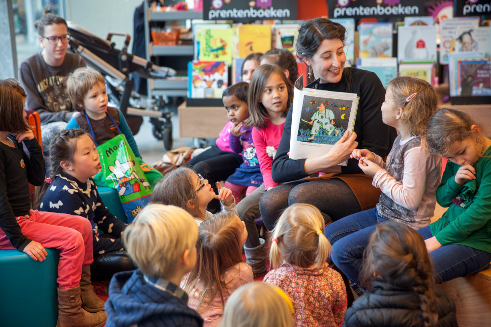 Mevrouw toont de kaft van een boek aan kinderen